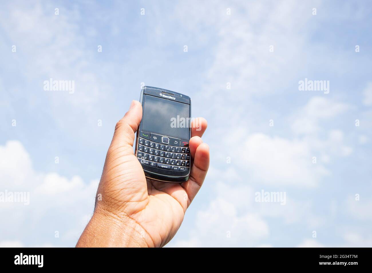 A hand is holding an outdated Blackberry smartphone up to the sky. Stock Photo