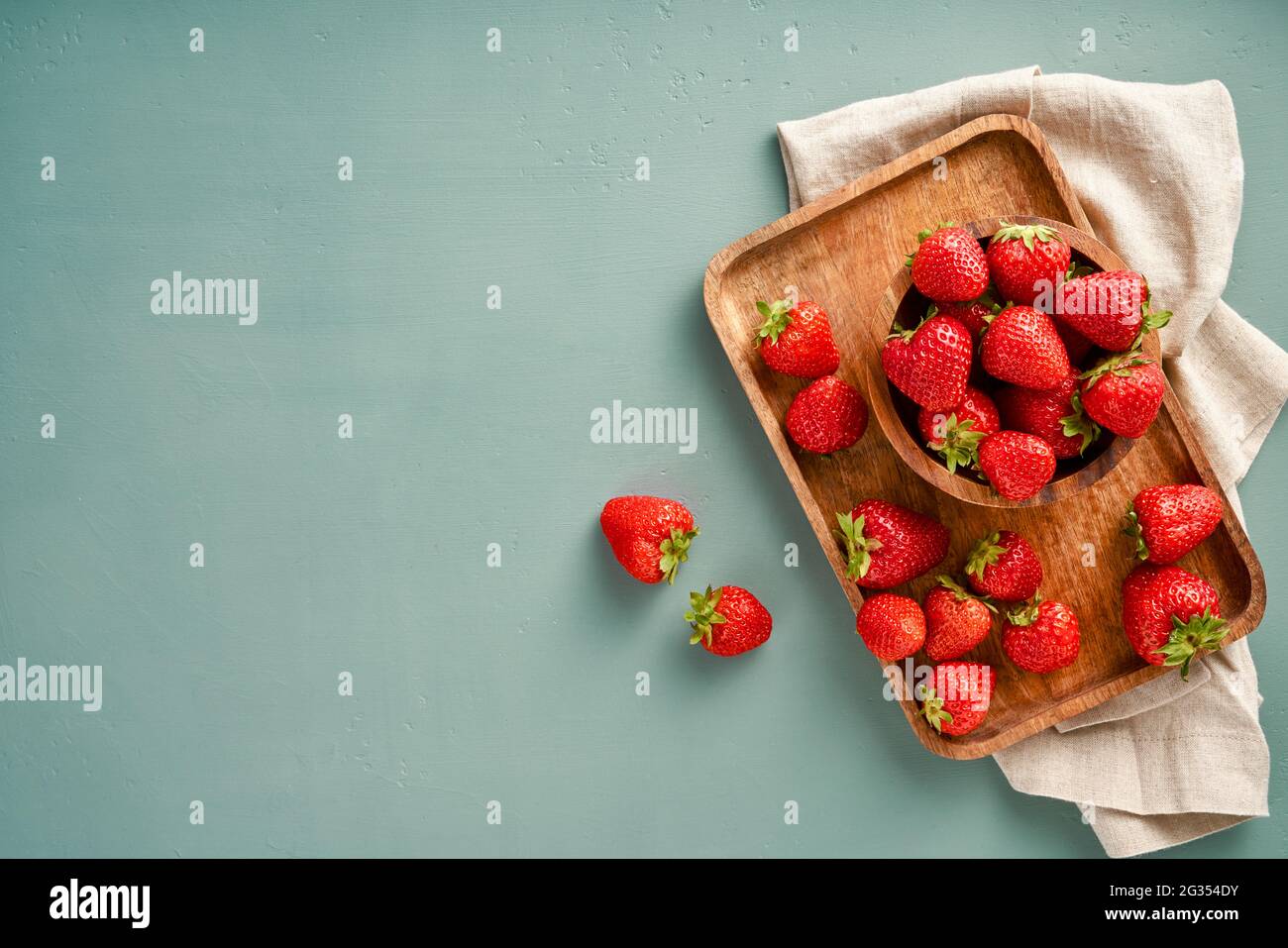 Fresh strawberry on a blue background with copy space. Top view of strawberries with leaves on wooden plate. Stock Photo