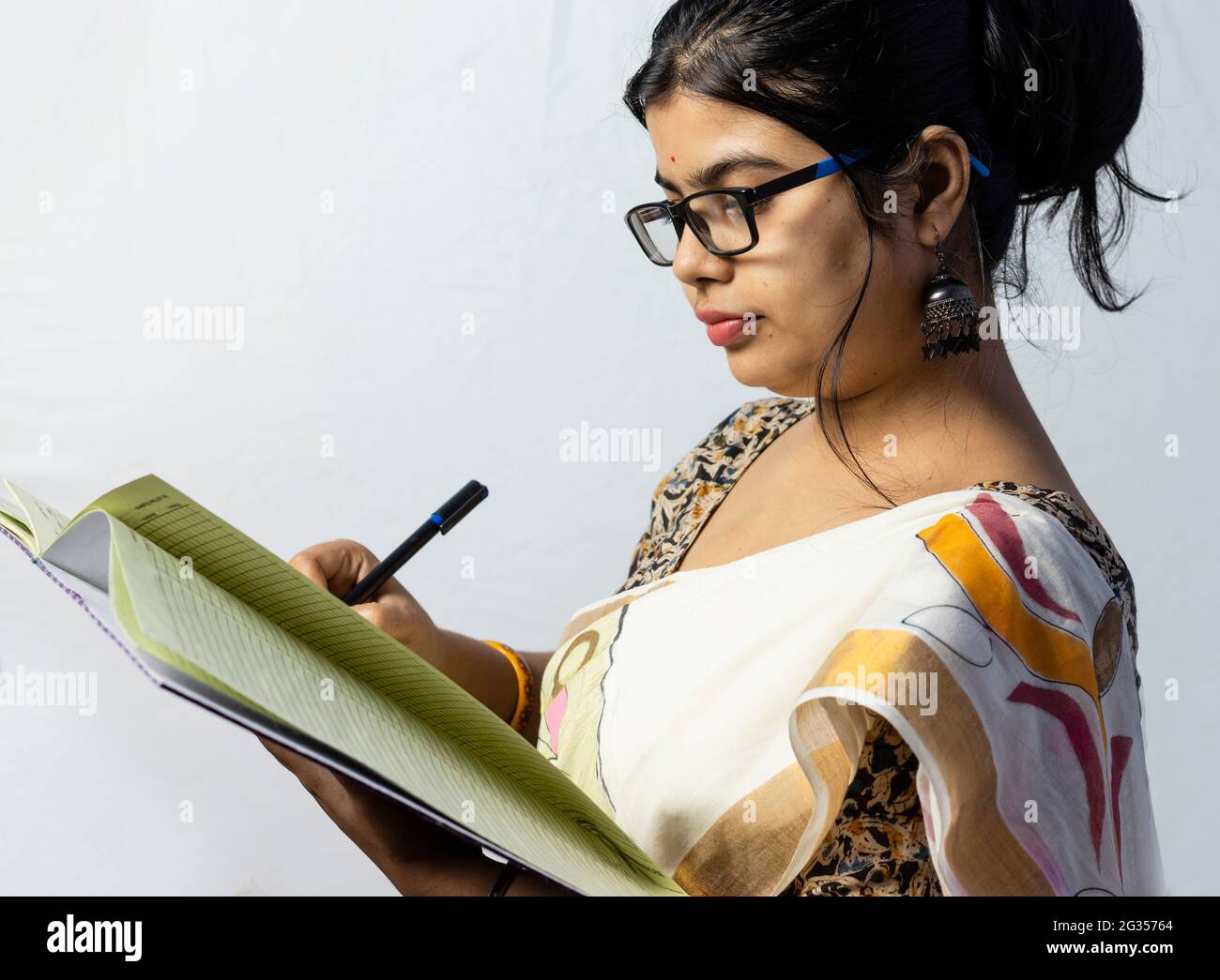 Isolated on white background an Indian office woman in saree writing on notebook with pen side facing Stock Photo