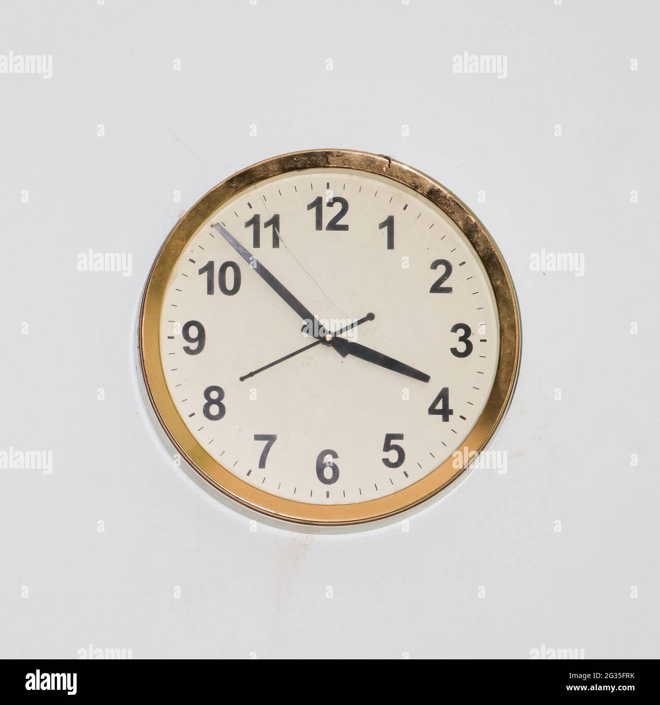 large round clock with an old, simple design and a gold frame hanging in a white wall showing accurate time Stock Photo