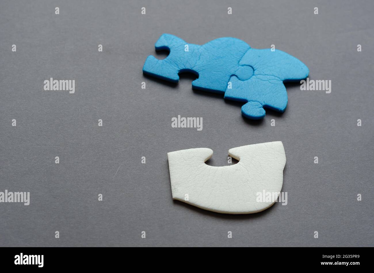 Blue and white puzzle piece on a gray background. Unconnected puzzle pieces. Side view from an angle. Selective focus. Stock Photo