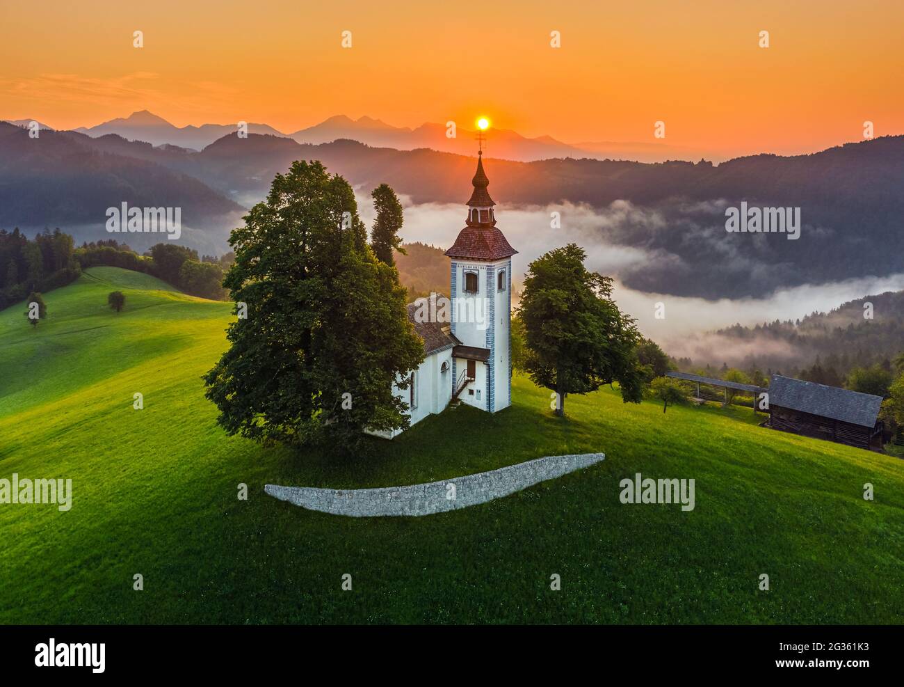 Sveti Tomaz, Slovenia - Aerial view of the beautiful hilltop church of Sveti Tomaz (Saint Thomas) with amazing golden foggy sunrise and the Julian Alp Stock Photo