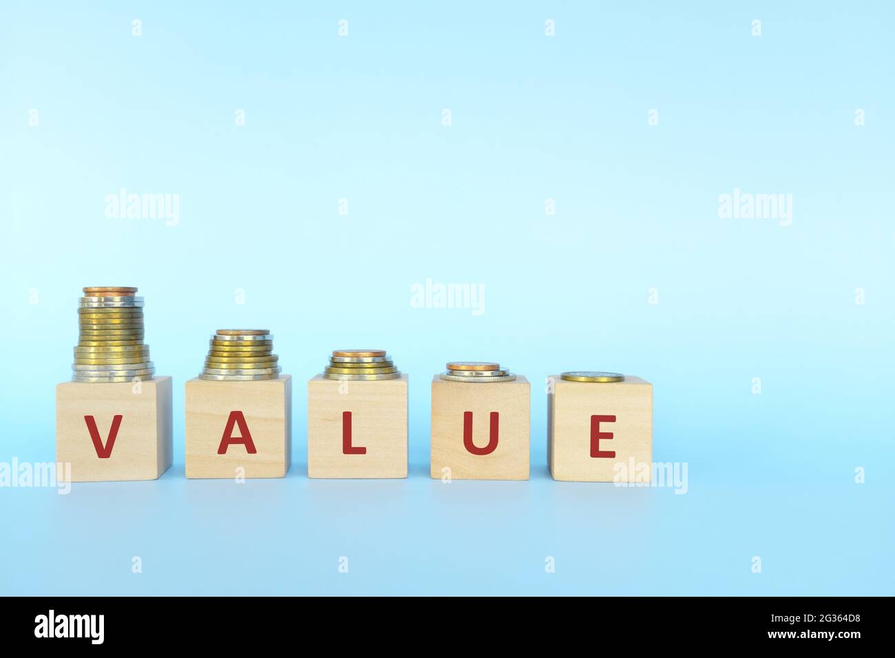 Price devaluation or value depreciation concept. Decreasing stack of coins in wooden blocks with word value. Stock Photo