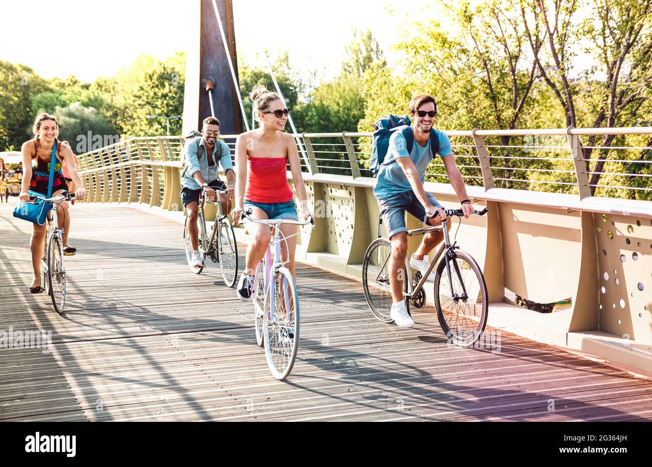 Happy milenial friends having fun riding bike at city park bridge - Life style concept with young hipster students biking together on bicycle lane Stock Photo