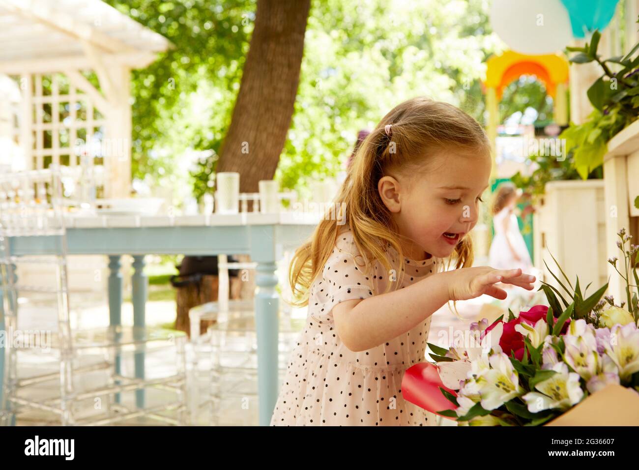 Side view of adorable little girl touching bouquet of flowers with interest in courtyard Stock Photo