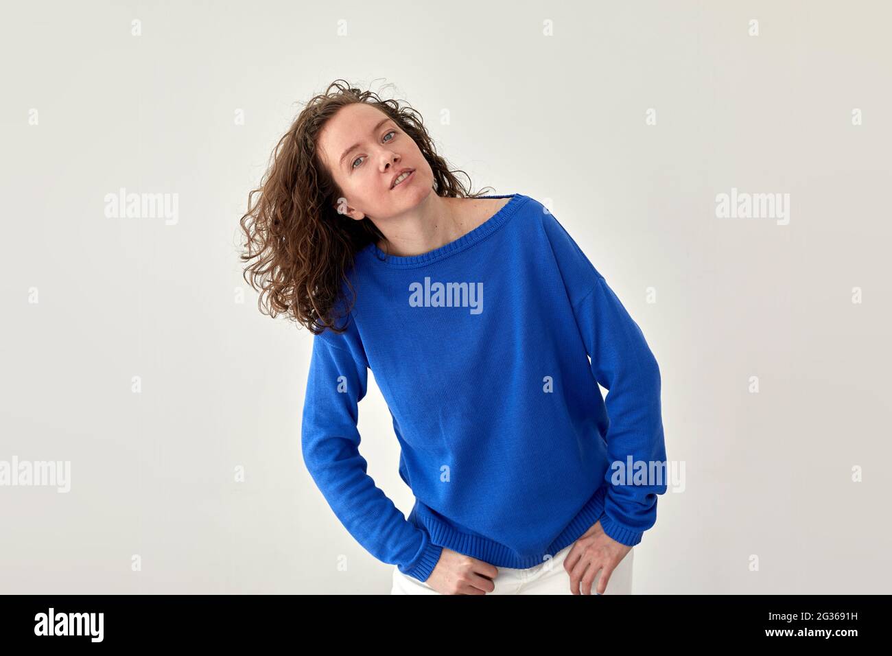 Young female model in trendy oversize blue woolen sweatshirt looking at camera against white background Stock Photo