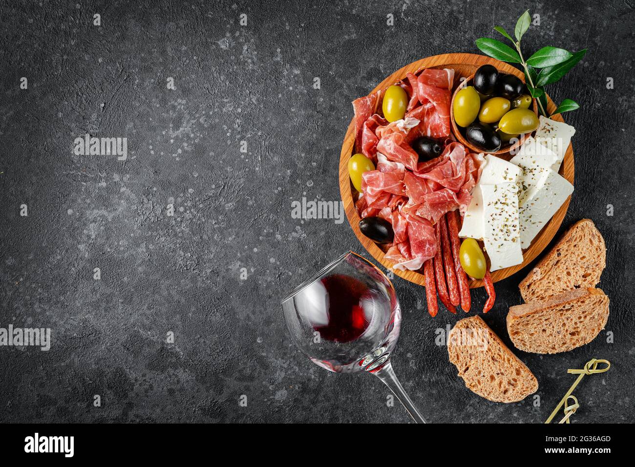 Appetizer wooden plate with meat, cheese and olives on dark concrete background. Copy space, flat lay. Stock Photo