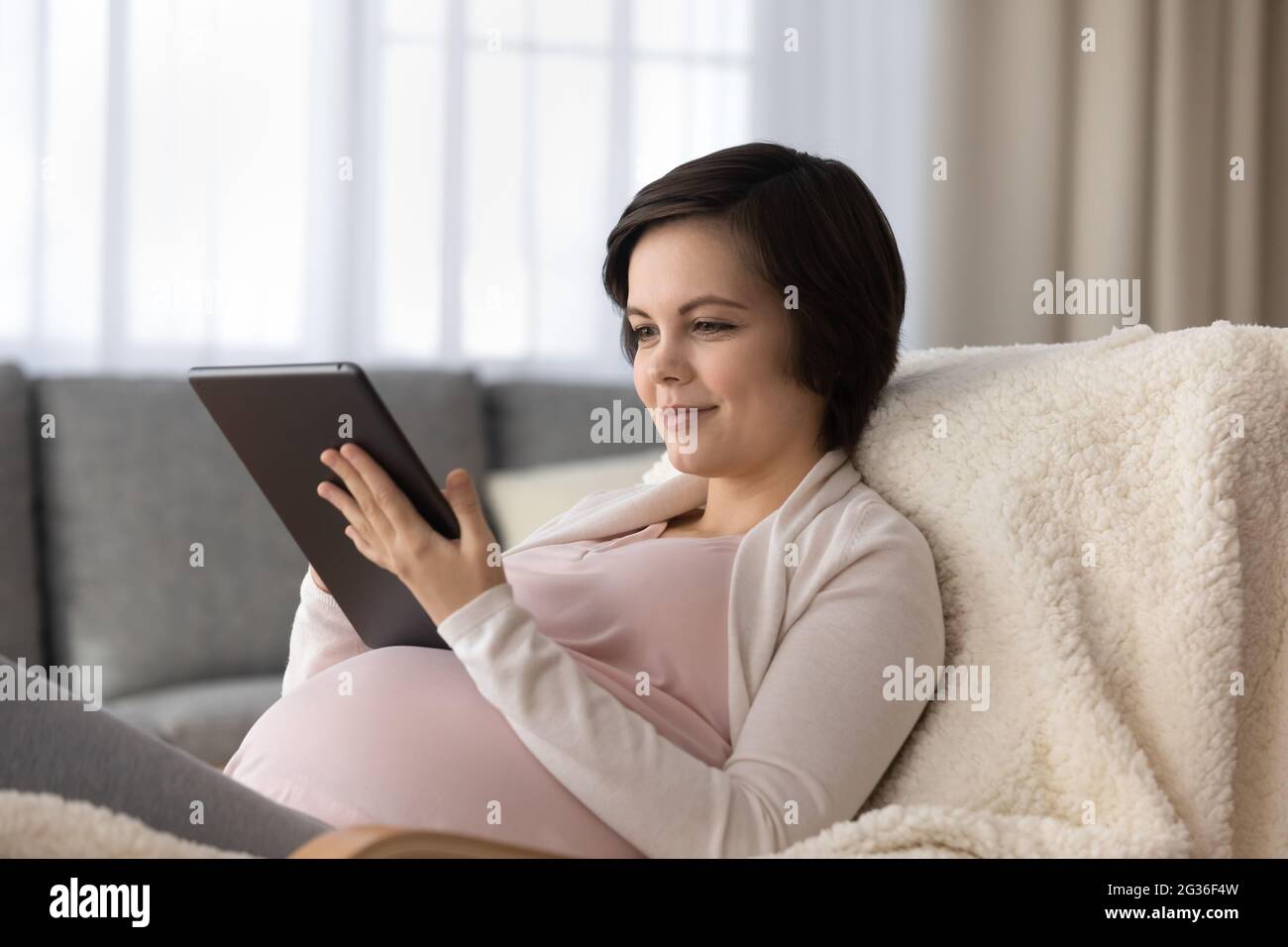Beautiful pregnant woman using tablet, relaxing with gadget at home Stock Photo
