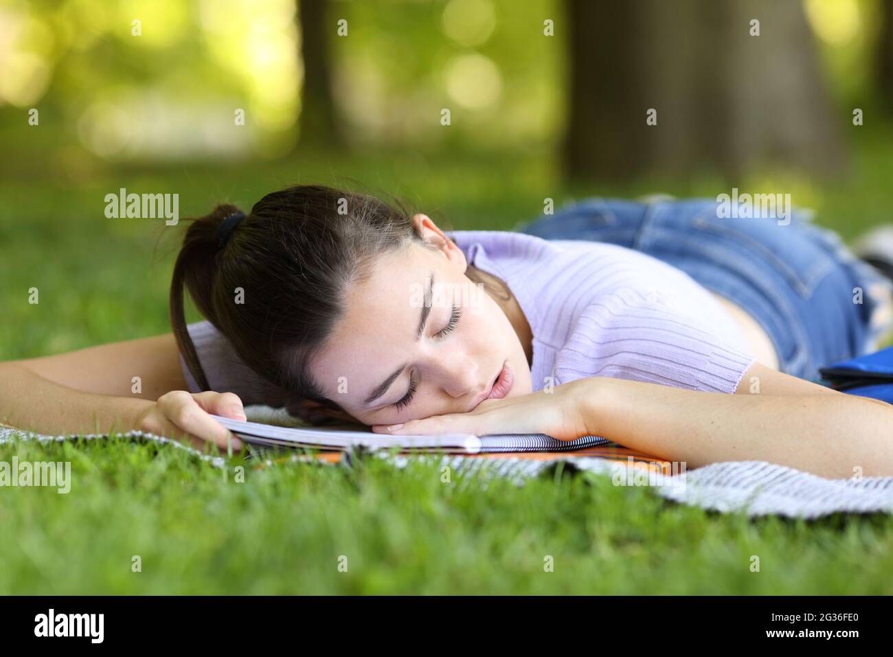 Tired student sleeping on notebook in a park or campus Stock Photo