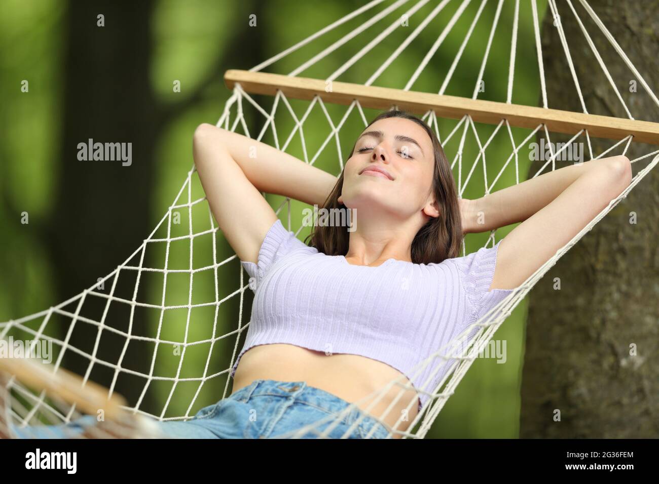 Relaxed woman on summer vacation resting on rope hammock in a forest Stock Photo