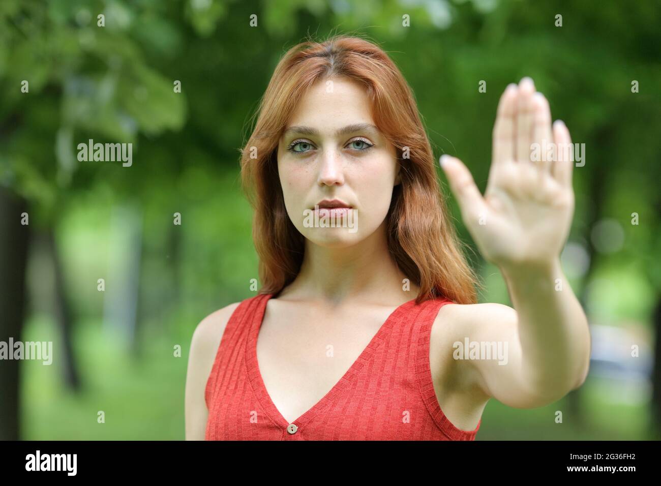 Serious redhead woman gesturing stop with her hand standing in a park Stock Photo