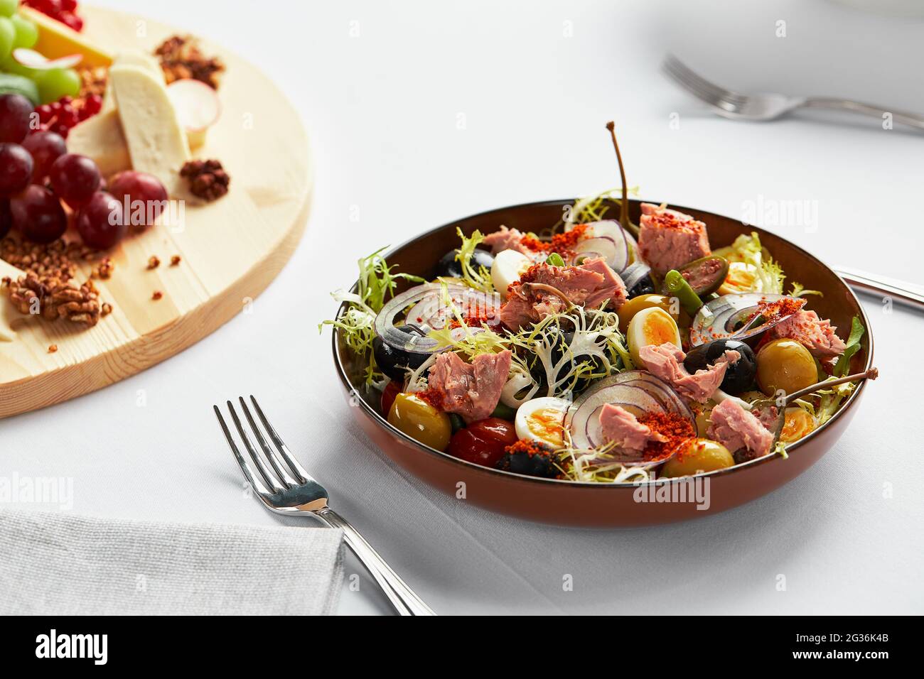 Fish salad on a light background, classic nicoise with large pieces of tuna fillet, eggs, olives and onions. Stock Photo