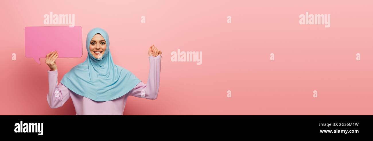 happy muslim woman with blue speech bubble looking at camera on pink ...