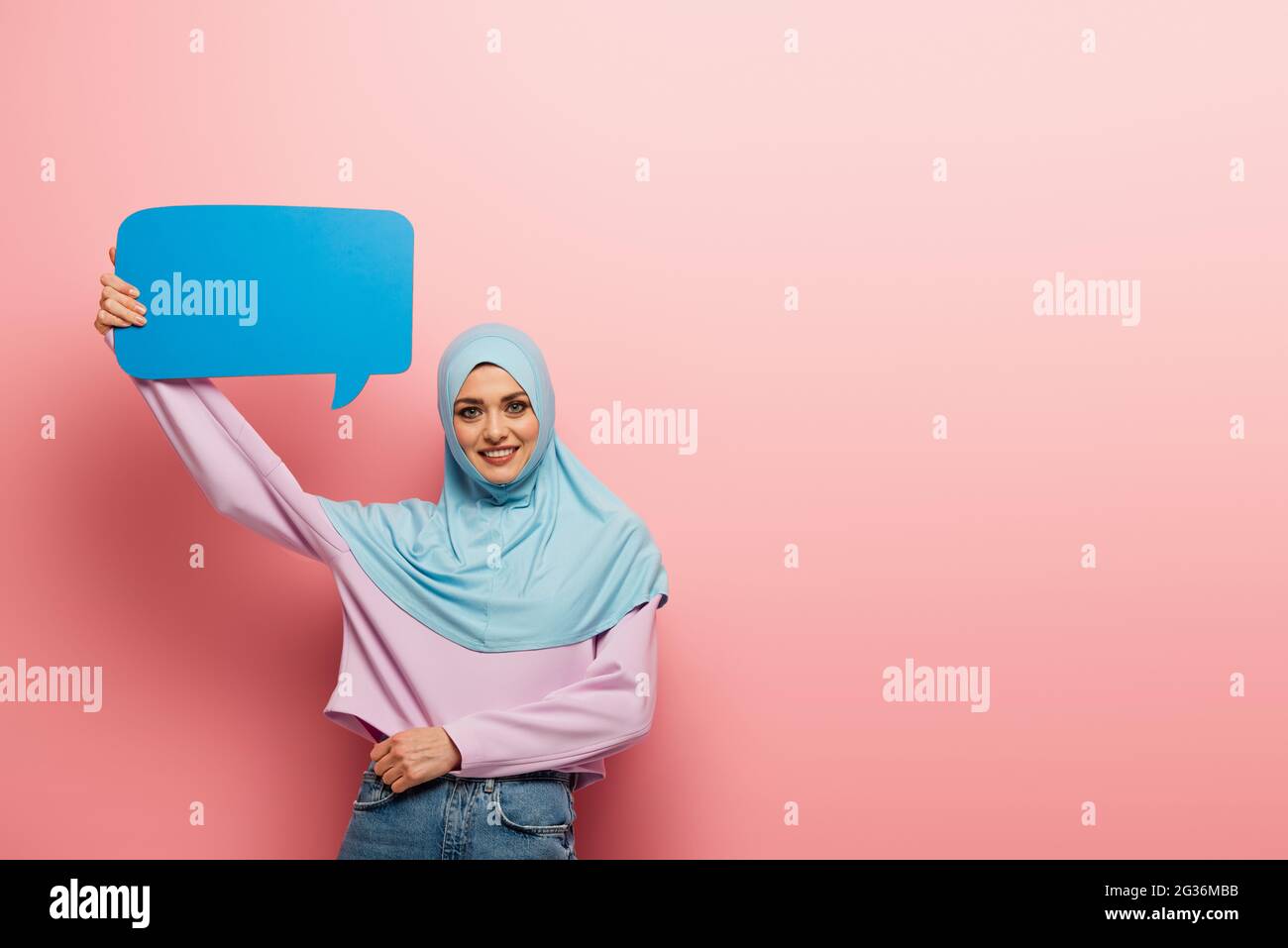 joyful arabian woman in blue hijab holding speech bubble on pink ...
