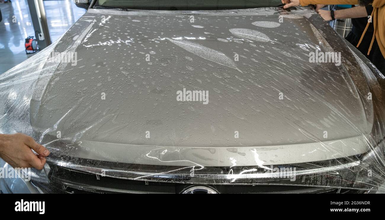Process of armoring car hood with transparent polyurethane anti-gravel film cover coating or PPF in car detailing studio garage. Stock Photo
