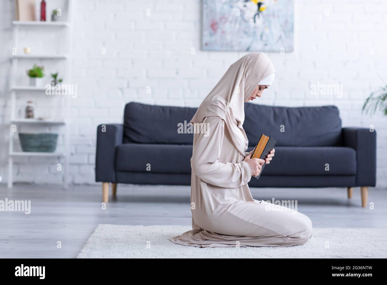 side view of muslim woman praying with koran on floor at home Stock Photo