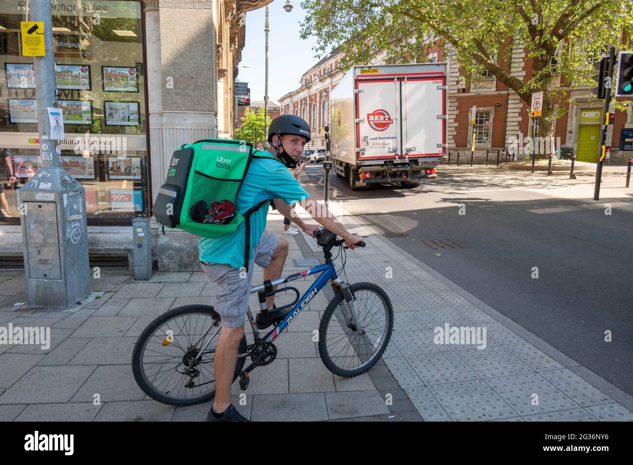 Uber eats take away  delivery man on a bicycle waiting at a pedestrian crossing in norwich city centre Stock Photo
