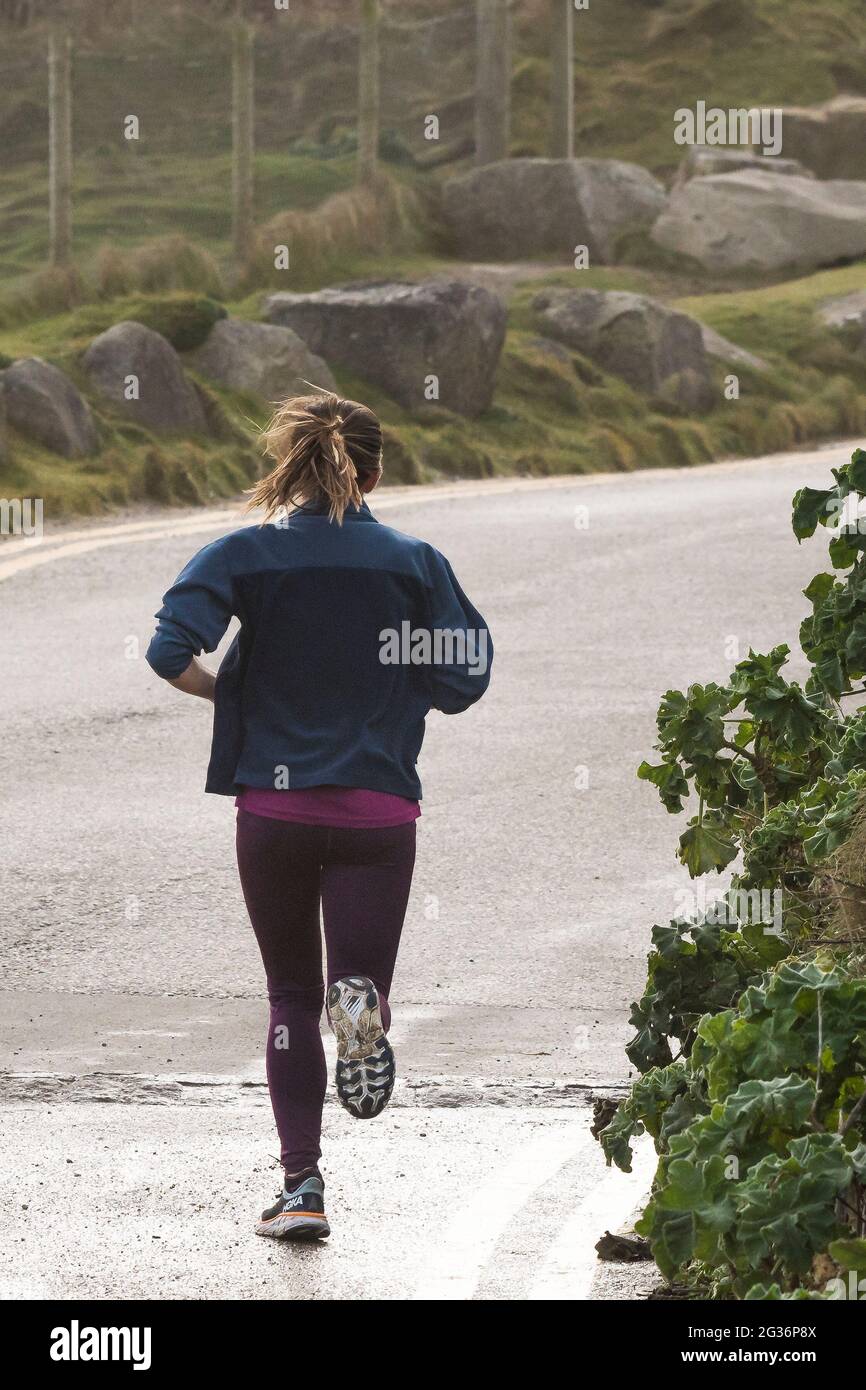 A rear view of a young woman running on a road in Newquay in Cornwall. Stock Photo