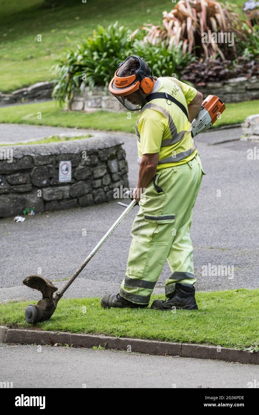 A Cormac worker strimming grass in Trenance Gardens in Newquay in Cornwall. Stock Photo