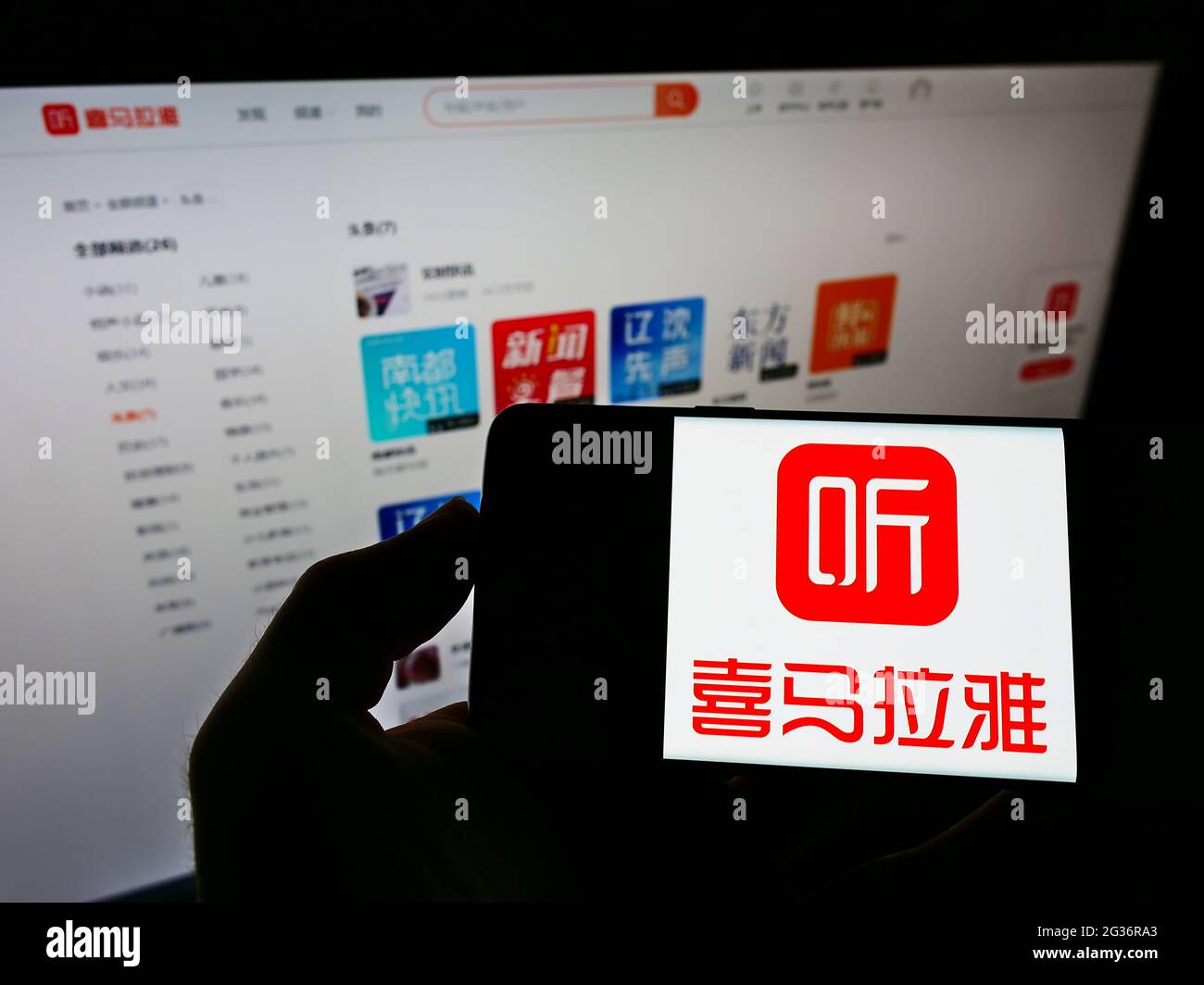 Person holding cellphone with business logo of Chinese online radio platform Ximalaya on screen in front of webpage. Focus on phone display. Stock Photo