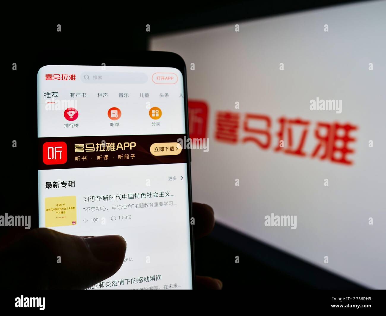 Person holding cellphone with company webpage of Chinese online radio platform Ximalaya on screen in front of logo. Focus on center of phone display. Stock Photo