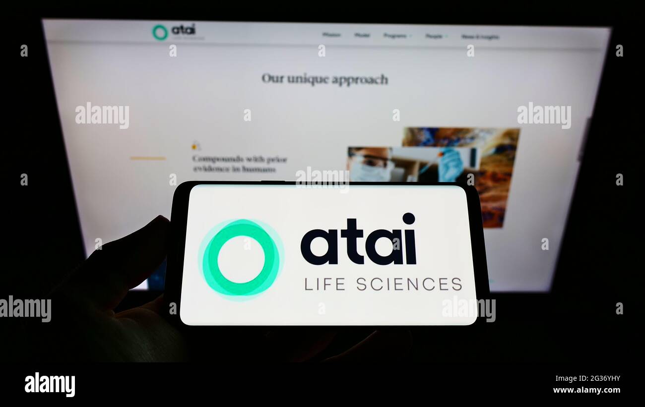 Person holding cellphone with logo of German biotech company ATAI Life Sciences AG on screen in front of business web page. Focus on phone display. Stock Photo