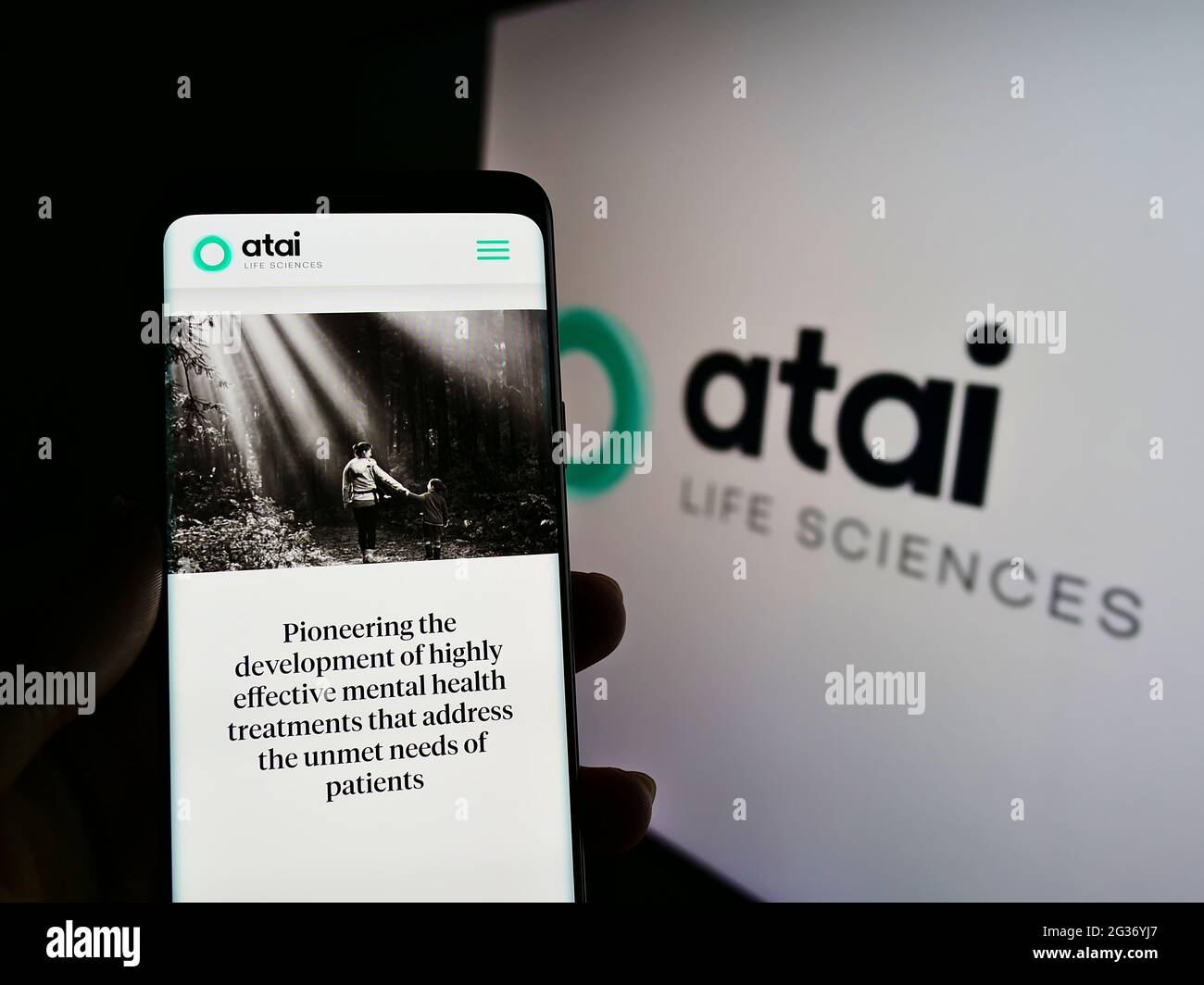 Person holding smartphone with website of German biotech company ATAI Life Sciences AG on screen in front of logo. Focus on center of phone display. Stock Photo