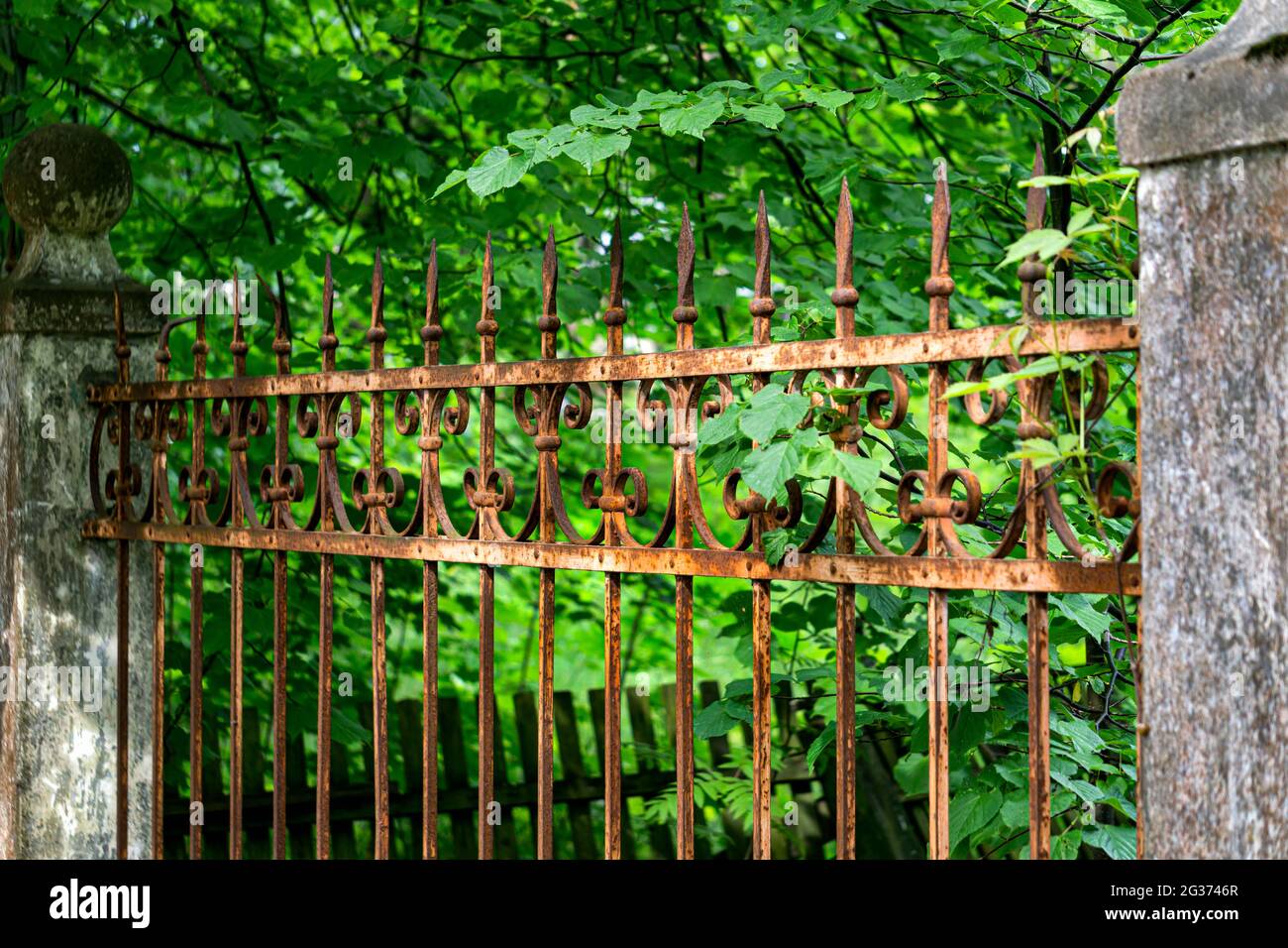 There is an old forged, rusty fence between the concrete pillars. Stock Photo