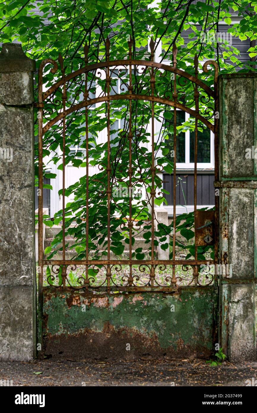 There is an old forged, rusty fence between the concrete pillars. Stock Photo