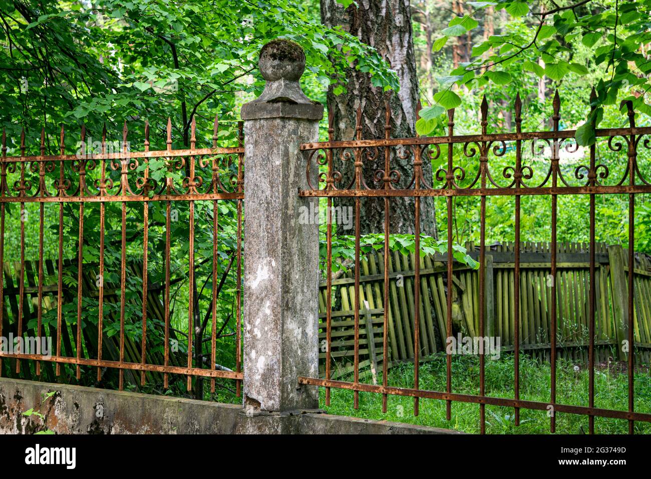 There is an old forged, rusty fence between the concrete pillars. Stock Photo