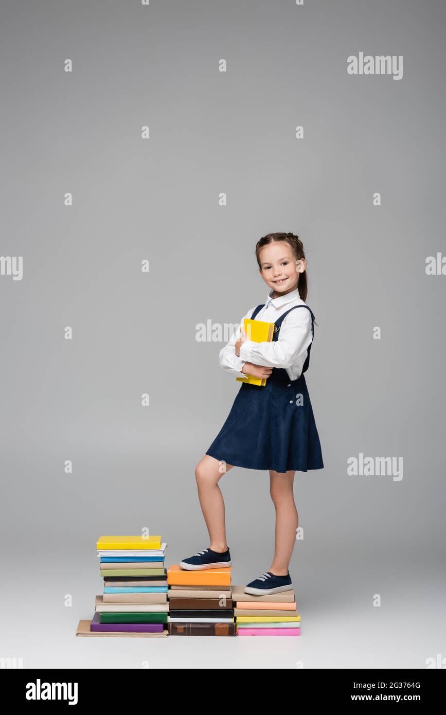 happy schoolgirl standing on pile of books on grey Stock Photo - Alamy