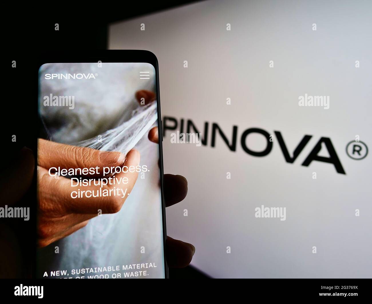Person holding cellphone with website of Finnish fiber textile company Spinnova Plc on screen in front of logo. Focus on center of phone display. Stock Photo