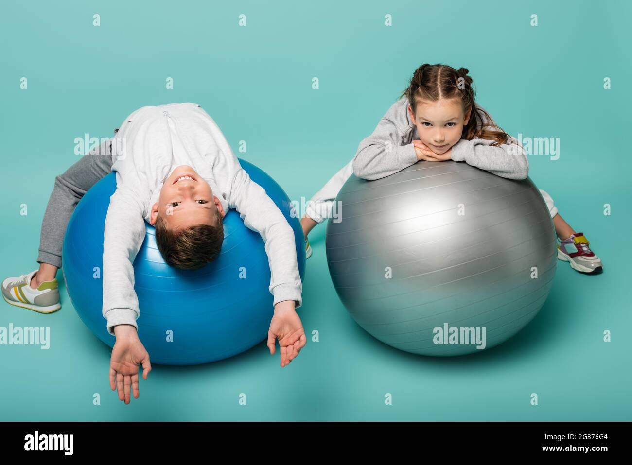 Cheerful little girl wearing sport clothes doing exercises with fitness  ball isolated over blue background Stock Photo - Alamy
