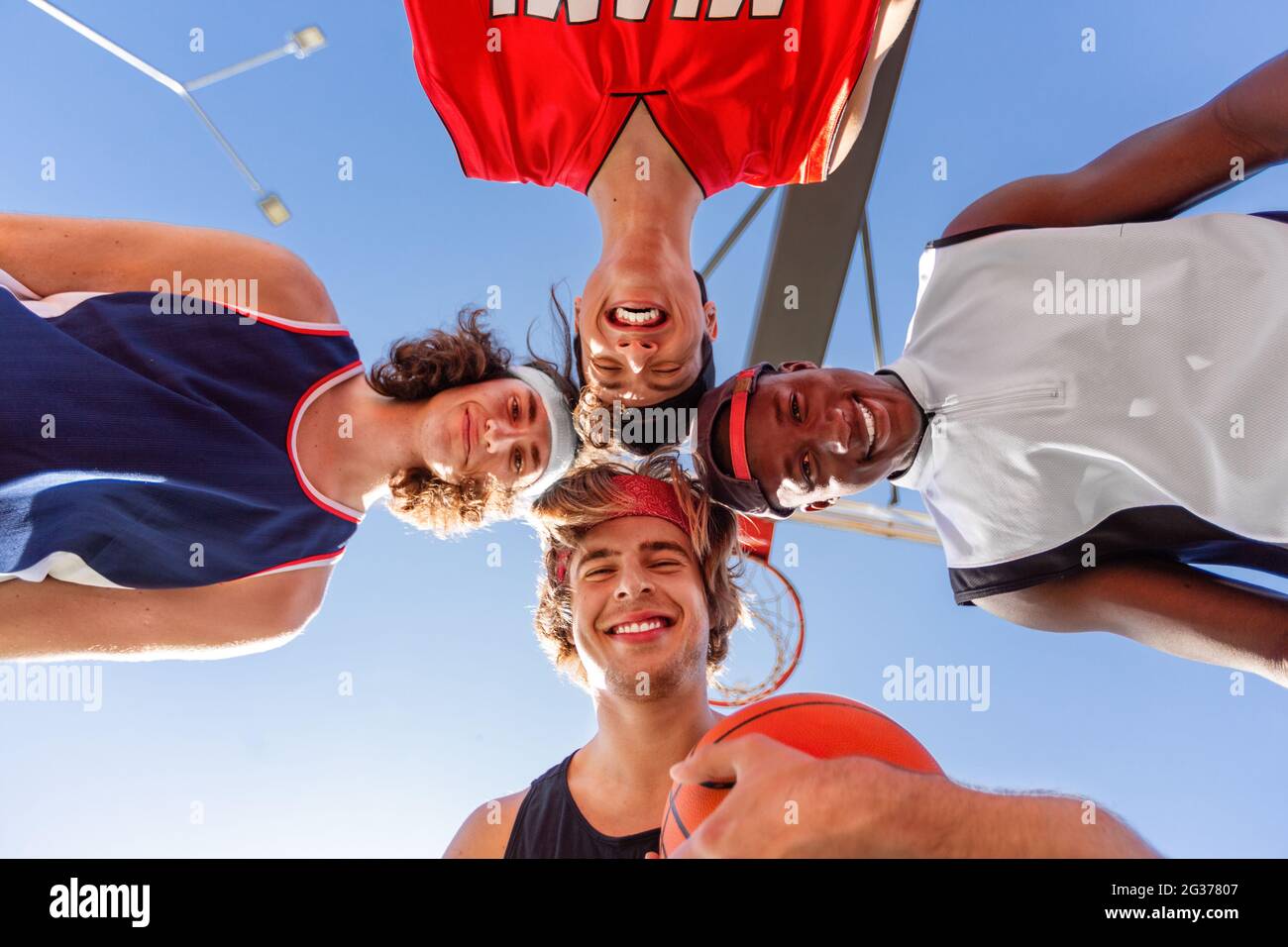 Group of happy basketball players putting their heads together in unity outdoors, bottom view