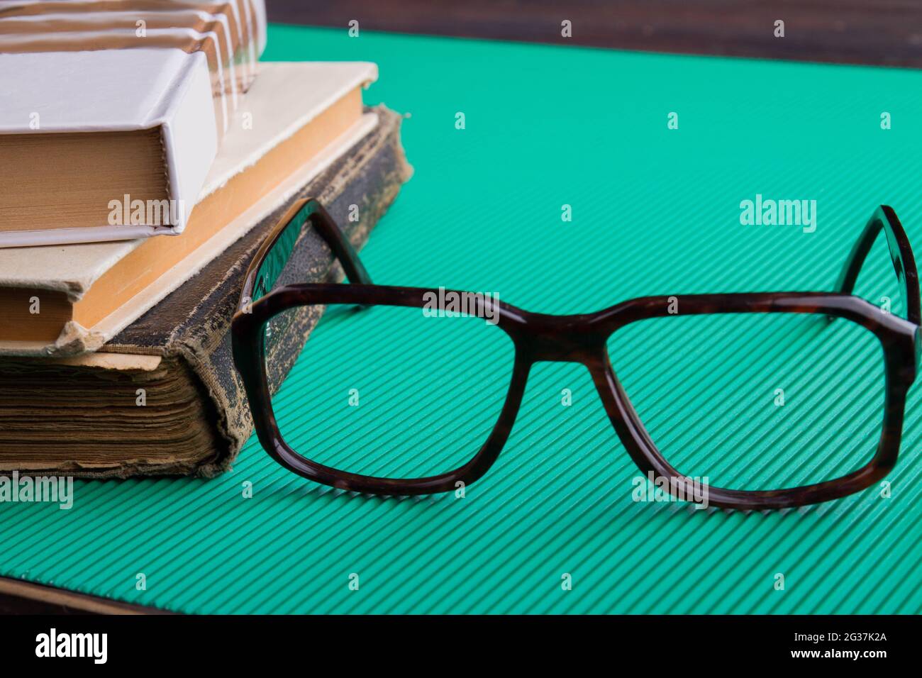 Close-up glasses and stack of old books on green background. Stock Photo