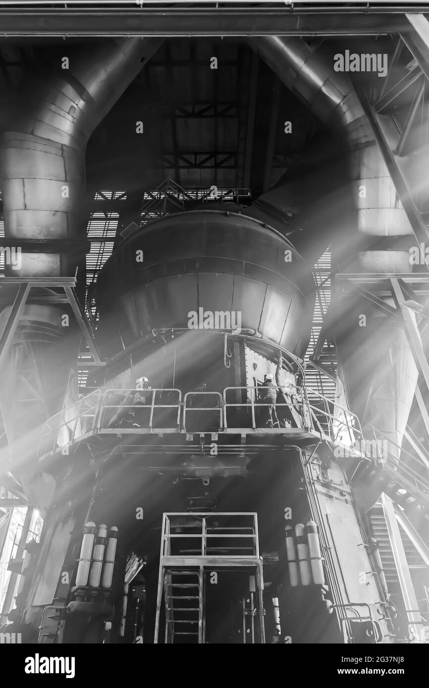 Two male engineers wearing protective equipment check and repairing large machine in a factory. focus on the largest machine. Stock Photo