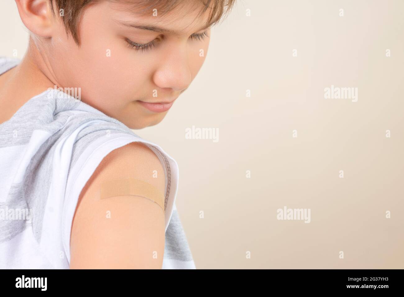 Teenage boy with adhesive bandage plaster on his arm after vaccination. Injection covid vaccine, healthcare for children and teenagers Stock Photo