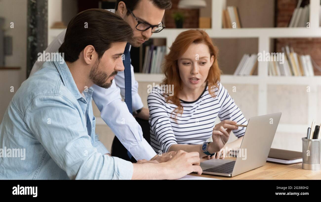 Concentrated three millennial employees preparing presentation on computer. Stock Photo