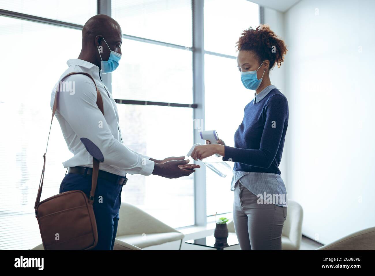 Two diverse business colleagues wearing face masks disinfecting hands and taking temperature Stock Photo