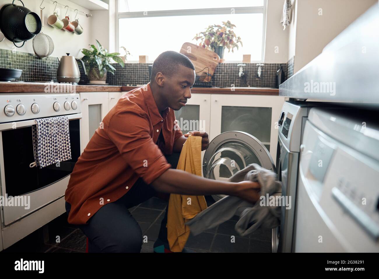 Young African man putting clothes in a washing machine at home Stock Photo
