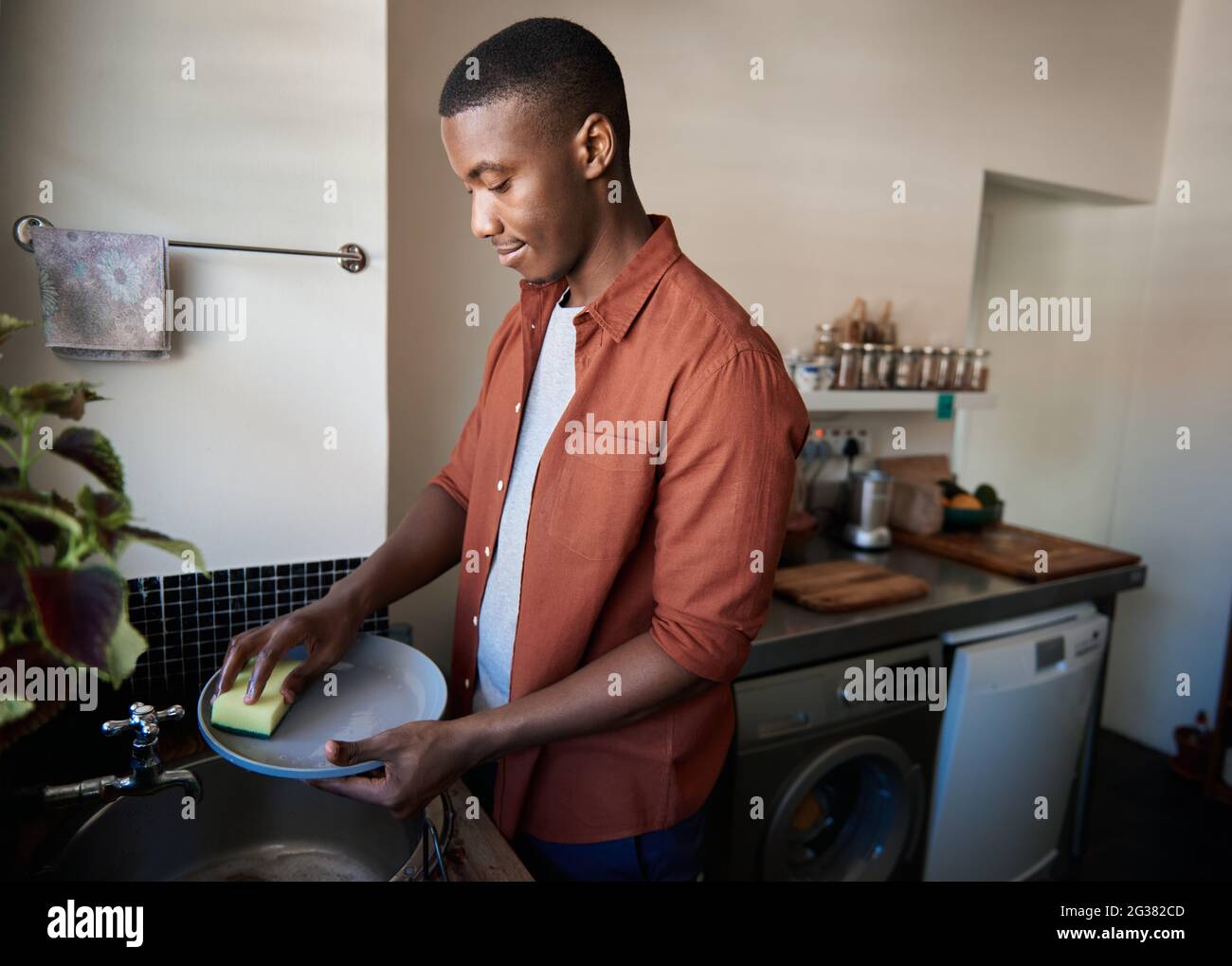 Young African man washing dishes in his kitchen at home Stock Photo