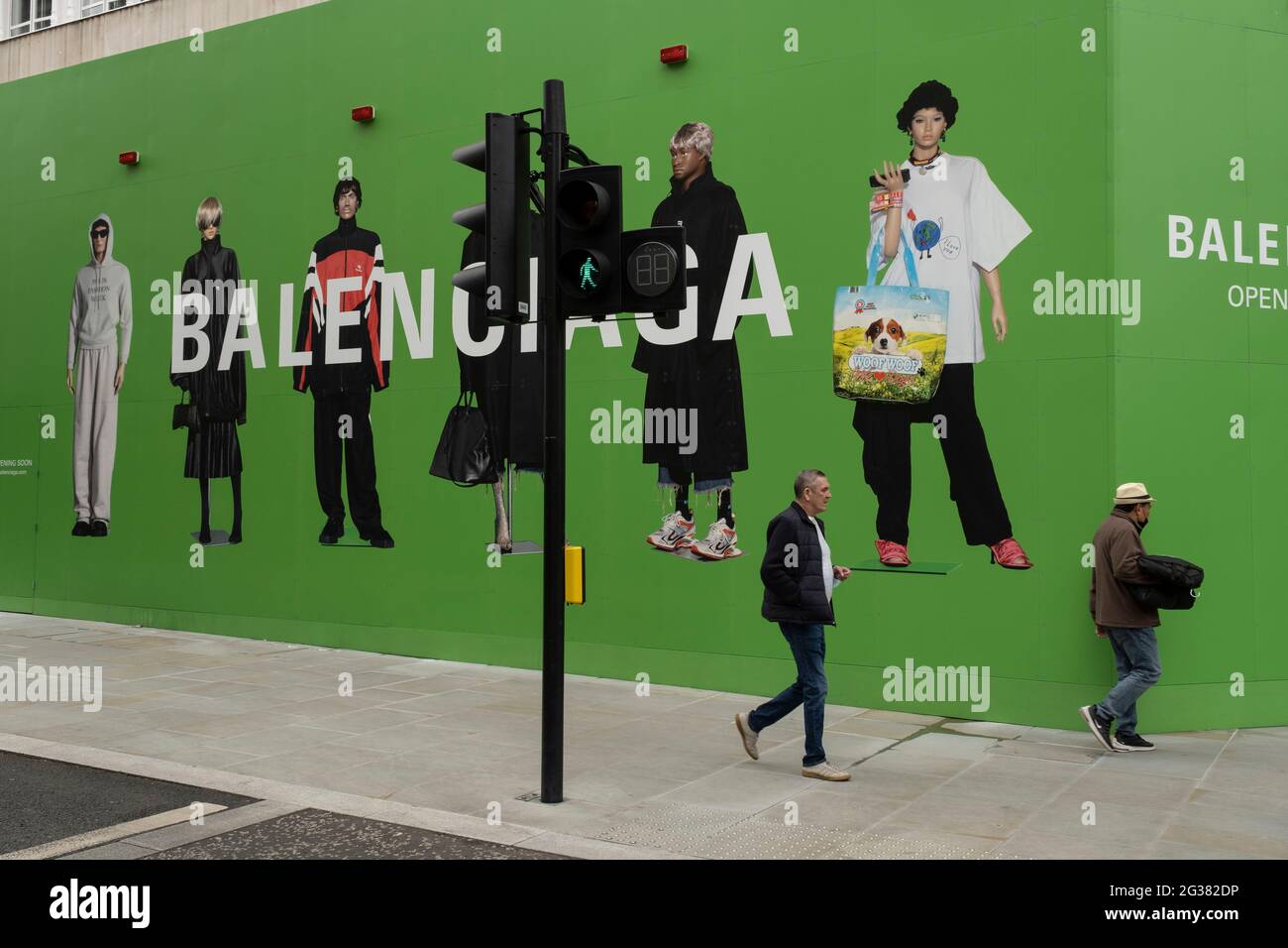 People interact with large scale action figures wearing fashionable  clothing against a huge green hoarding which covers the Balenciaga store  during a refit in the upmarket area on Bond Street on 25th