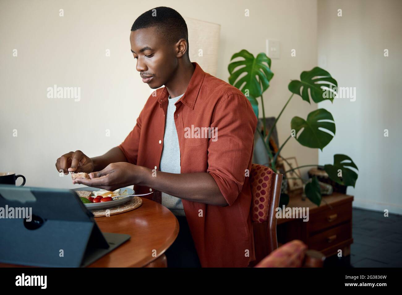 Young African man eating breakfast and using a digital tablet Stock Photo