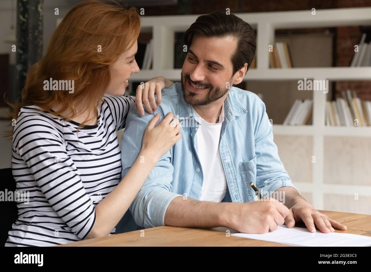 Happy bonding young family couple discussing offer, signing contract. Stock Photo