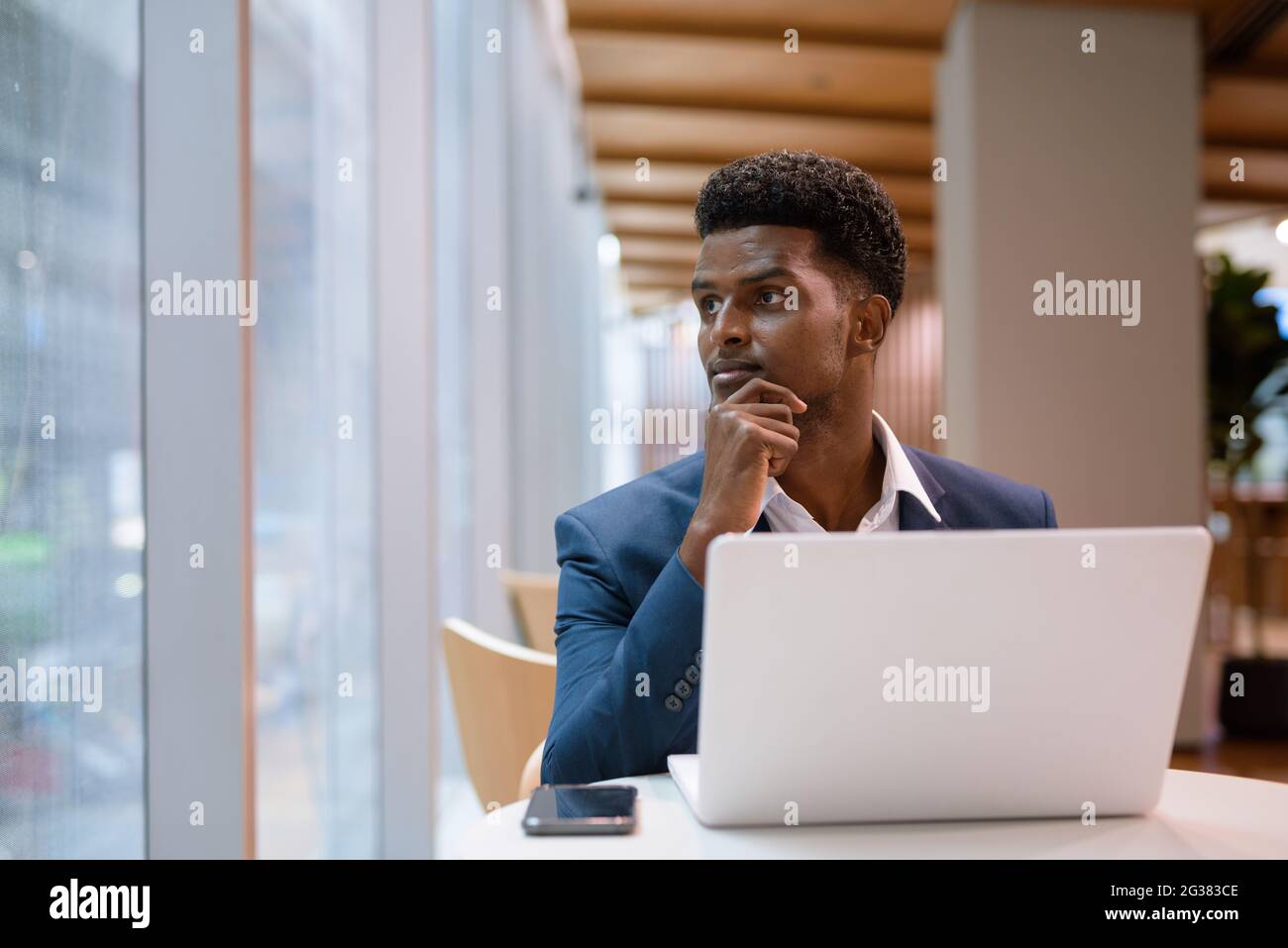 Portrait of African businessman using laptop computer in coffee shop while looking through window horizontal shot Stock Photo