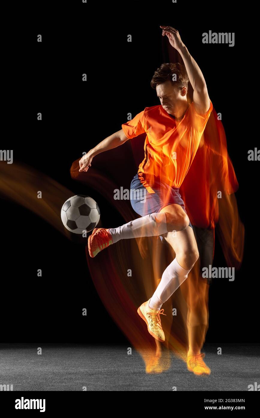 Young caucasian male football or soccer player kicking ball for the goal in mixed light on dark background. Concept of healthy lifestyle, professional Stock Photo