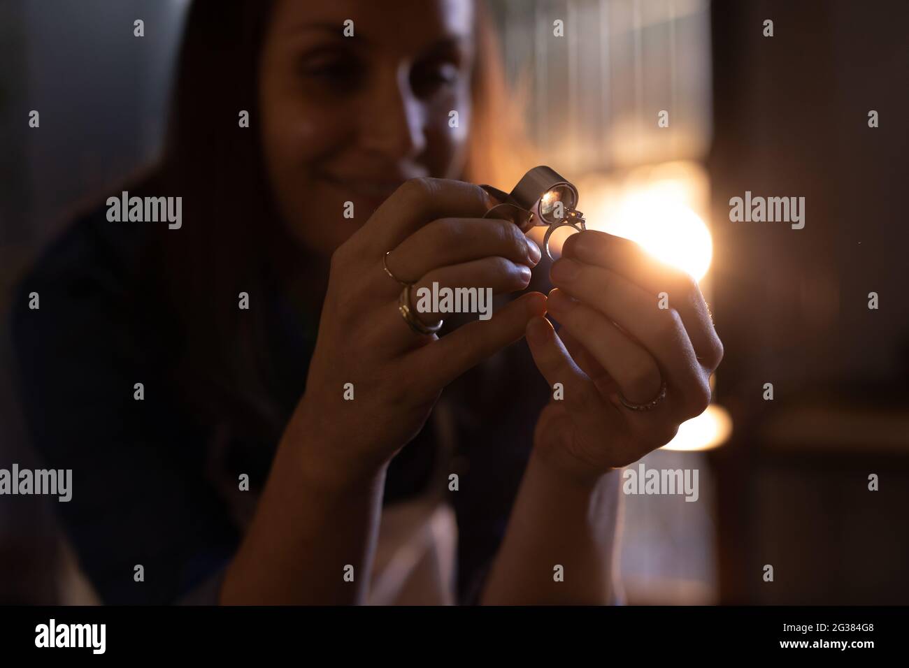 Caucasian female jeweller in workshop using magnifying glass to inspect ring Stock Photo