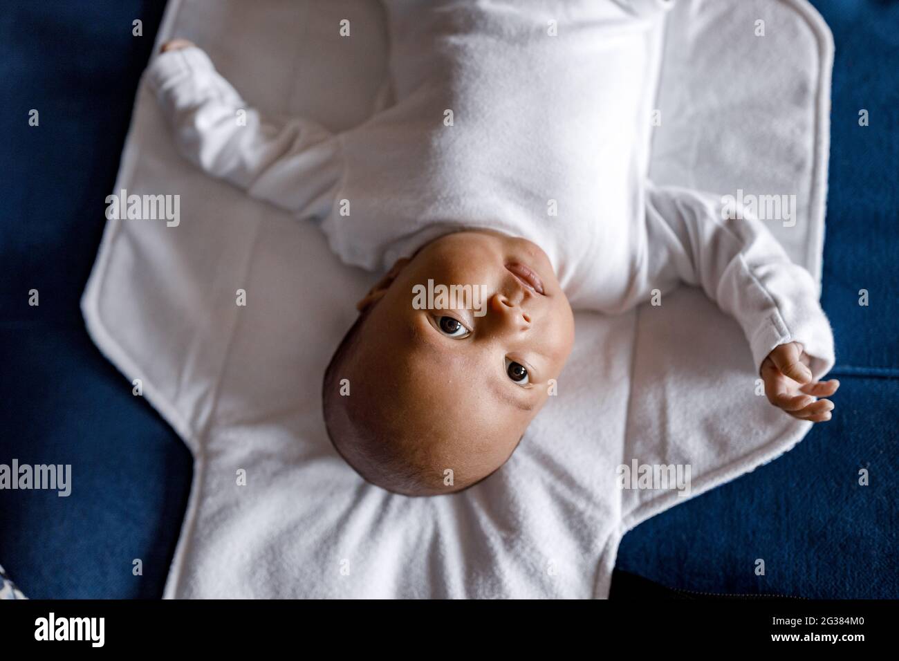Top view of newborn Afro American baby boy looking at camera and laying with blanket on sofa, while mother changes clothes and diapers. African Stock Photo