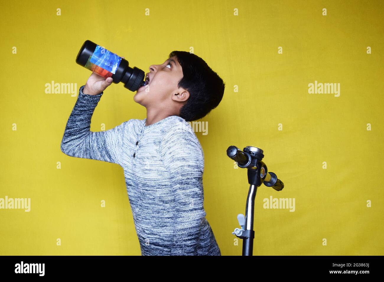 Indian little boy on a scooter drinking water on a yellow background