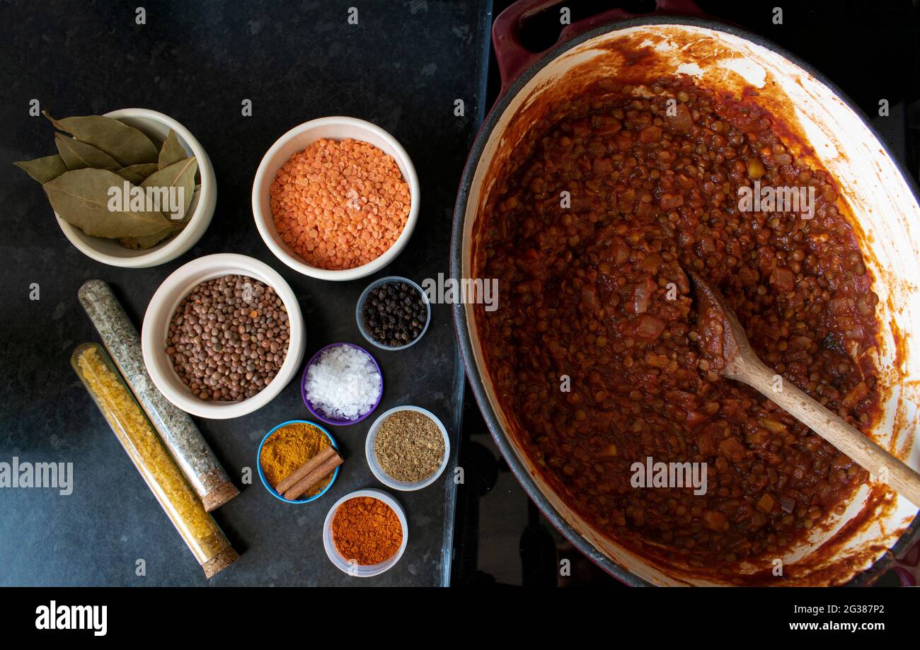Colorful cooking ingredients and spices next to a pot of hearty vegan lentil stew Stock Photo